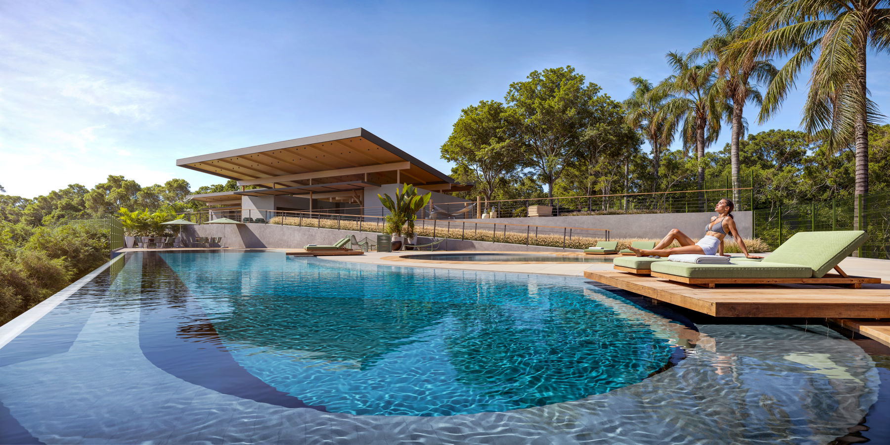 Vista aérea de lazer completo à beira do lago — pool deck, jardins e cabanas.
